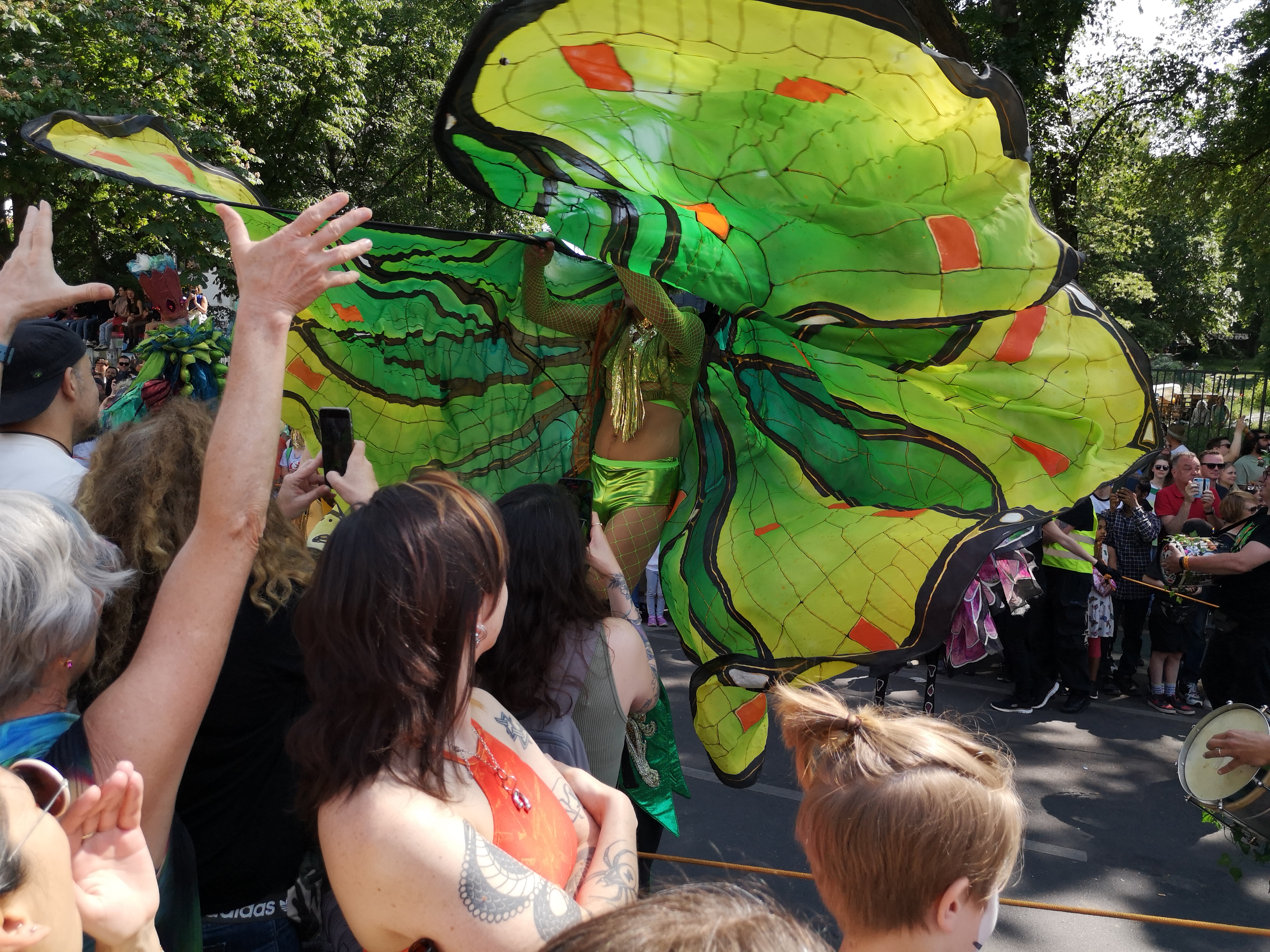 Foto von Stelzenläuferin im Schmetterlingskostüm beim Umzug vom Karneval der Kulturen am 28. Mai 2023 in Kreuzberg und in Neukölln in Berlin (Germany). Fotograf: Erwin Thomasius.