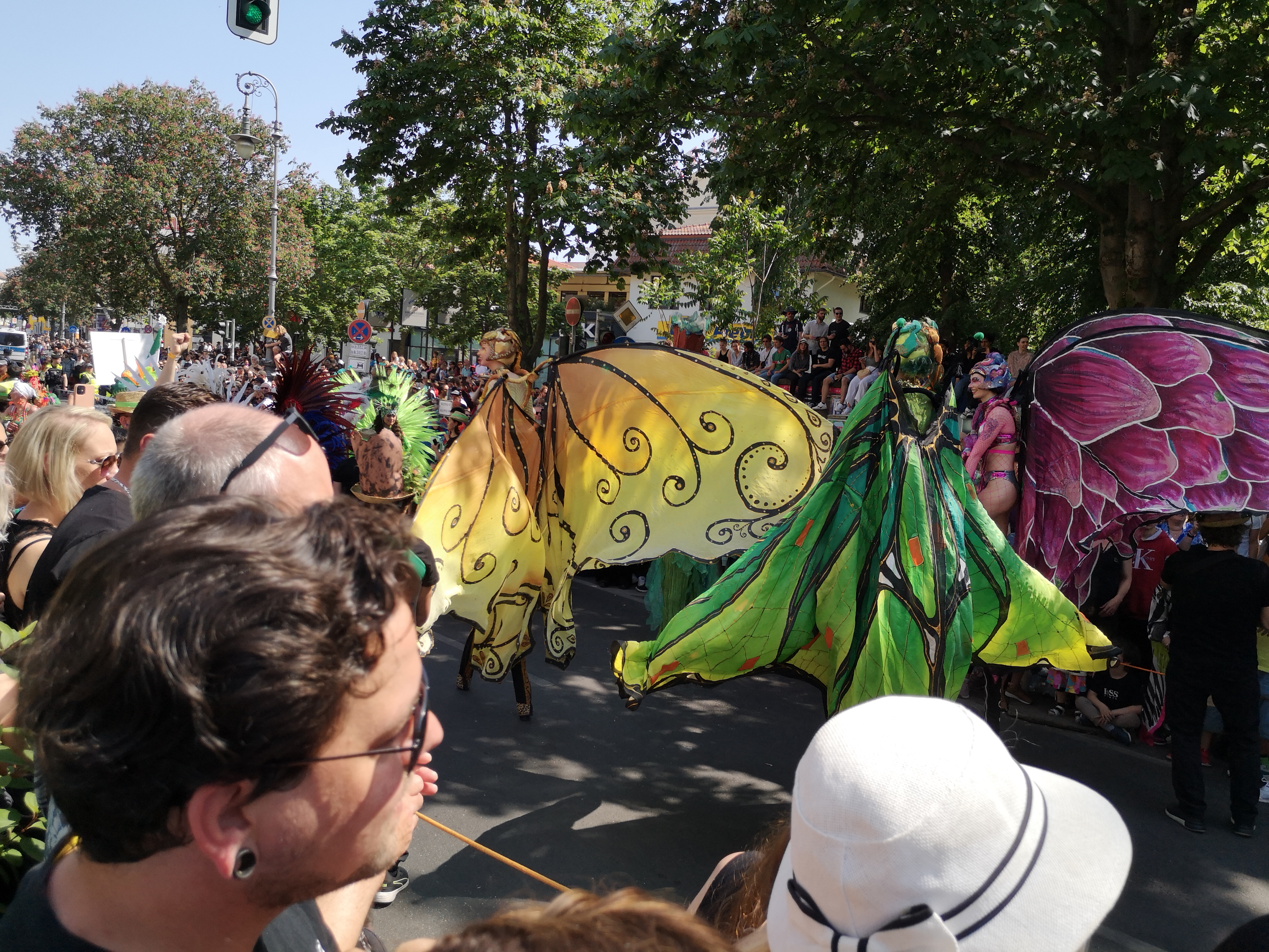 Foto von drei Stelzenläufern in Schmetterlingskostümen beim Umzug vom Karneval der Kulturen am 28. Mai 2023 in Kreuzberg und in Neukölln in Berlin (Germany). Fotograf: Erwin Thomasius.